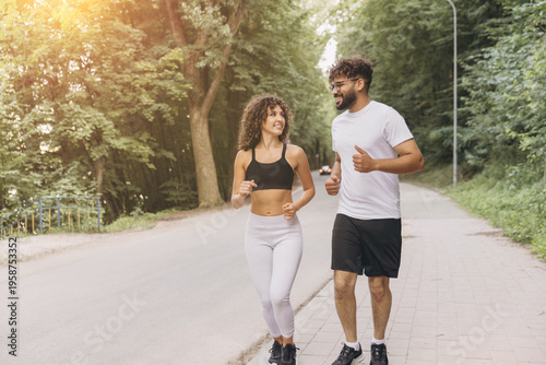 Happy diverse couple running on a path surrounded by green trees, actively pursuing health and wellness goals