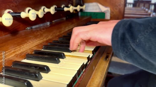 close up side view of hands of male organist playing church pipe organ keyboard