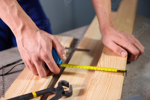 Obraz na płótnie Man measuring wooden plank with tape at grey table, closeup