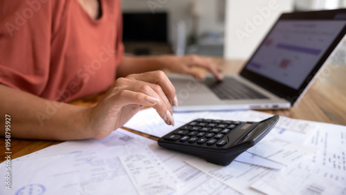 Close-up of female managing personal finances at home, using calculator and modern laptop surrounded by bills and receipts, as symbol of budgeting, accounting, and family expenses control. Accountancy