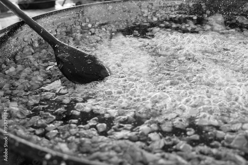 Close-up, black and white shot. Diced onions simmer in large pan. 