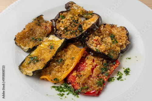 Obraz na płótnie Gratinated baked vegetables with breadcrumbs including eggplant zucchini and peppers served on white plate
