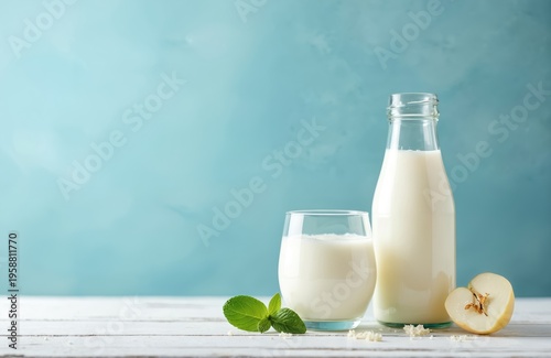 Glass and bottle of kefir or yogurt drink on white wood table. Fresh mint and quince slice next to beverage. Blue wall background and copy space.