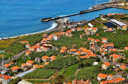 Aerial View of Coastal Village With Orange Roofs and Harbor Along Blue Sea Shoreline in Madeira