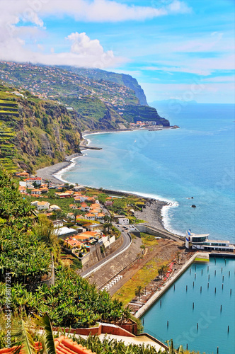 Cliffside Coastal Village Overlooking Calm Ocean, Curving Beach and Small Harbor on Sunny Day in Madeira