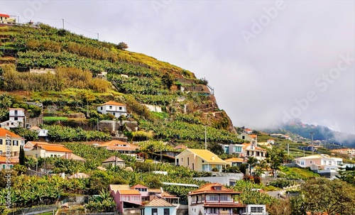 Scenic Coastal Road Along Cliff With Guardrail Overlooking Blue Ocean and Green Hills in Madeira.
