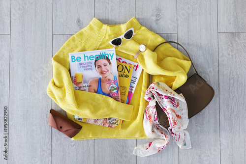 Lifestyle magazines, sweater and accessories on floor indoors, flat lay