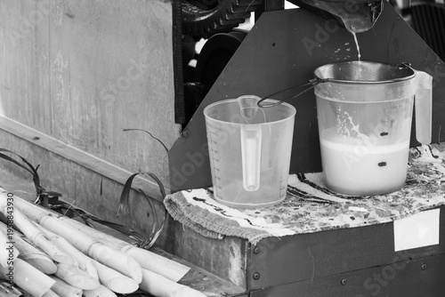 A close-up, eye-level shot captures fresh sugarcane juice dripping into a clear pitcher.