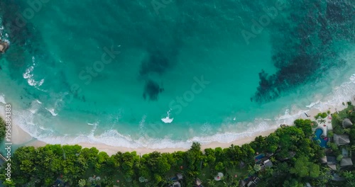 Crystal clear turquoise sea waves hitting the sandy beach, surrounded by green vegetation. Seychelles, Mahe.