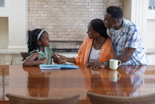 African American family leaning over polished wooden island in kitchen, reading picture book