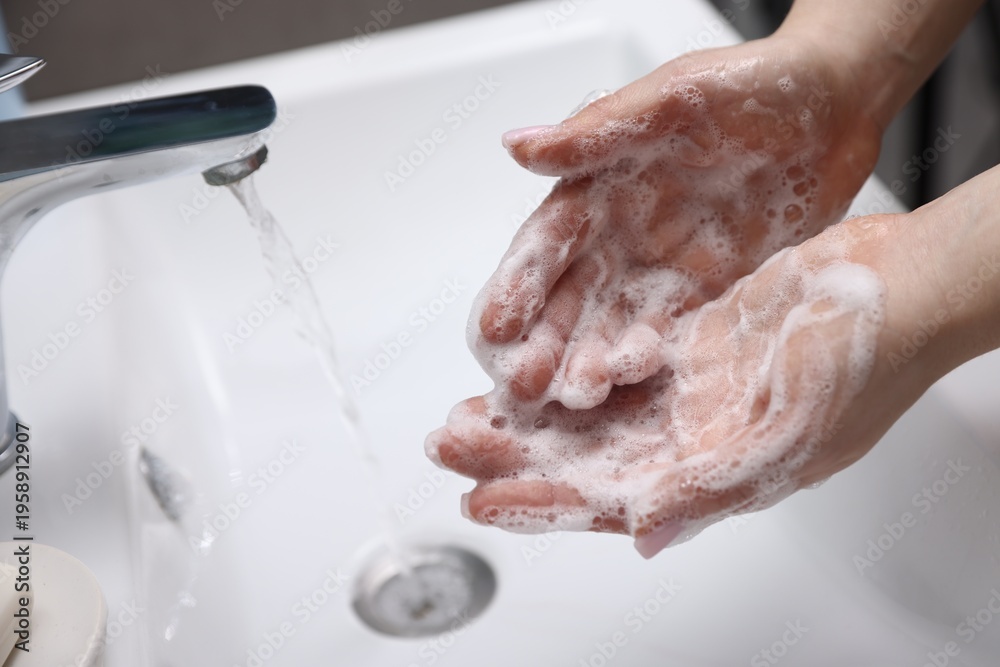 Fototapeta premium Woman washing hands with soap above white sink indoors, closeup