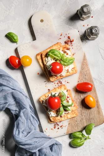 Tasty crackers with cheese, tomatoes and basil leaves on board on white grunge background