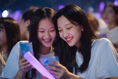 Enthusiastic Korean teenagers enjoying K-pop concert fan culture with light sticks and smartphones
