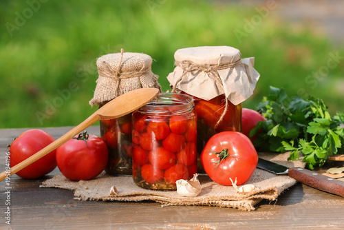 Jars of canned tomatoes with spoon and knife on wooden table outdoors