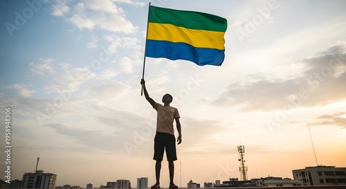 A person holding the flag of Gabon against a dramatic sky at sunset.