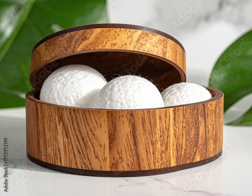 Wooden round container holds white spheres, framed by leaves on marble