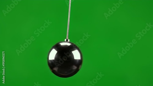 A polished, dark, egg-shaped object hangs from a thin wire against a green background