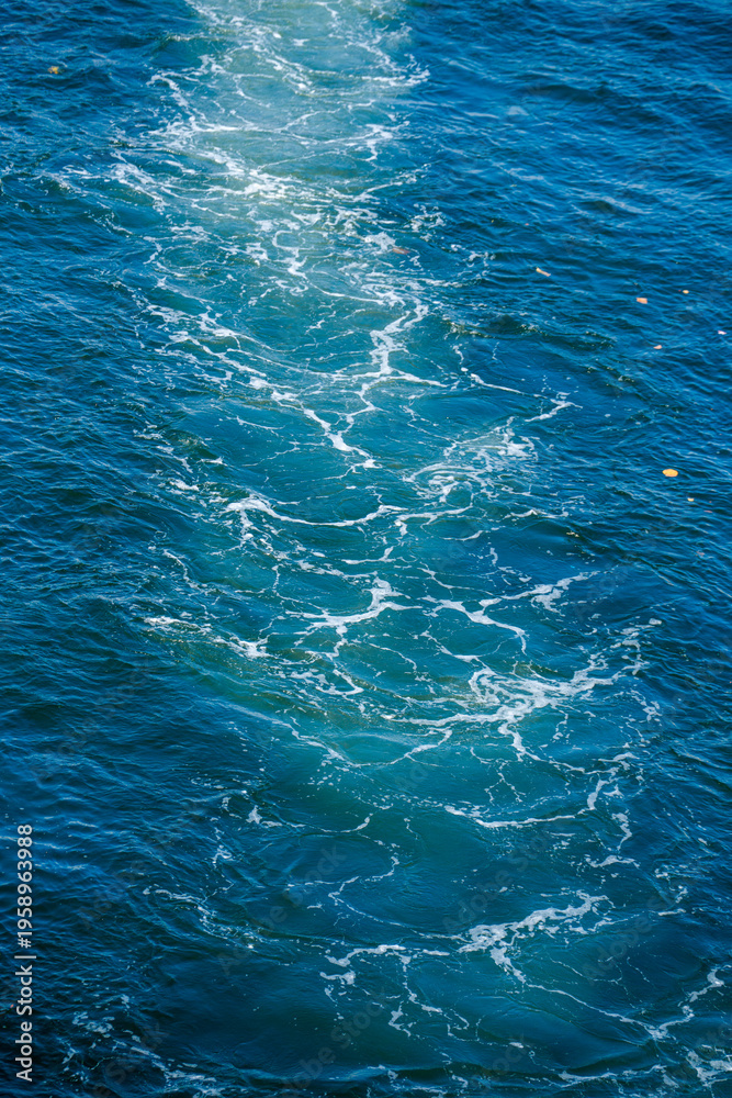 Fototapeta premium Strong white boat wake and foamy trail on the surface of deep blue ocean water under a bright sunny sky in a tropical resort.