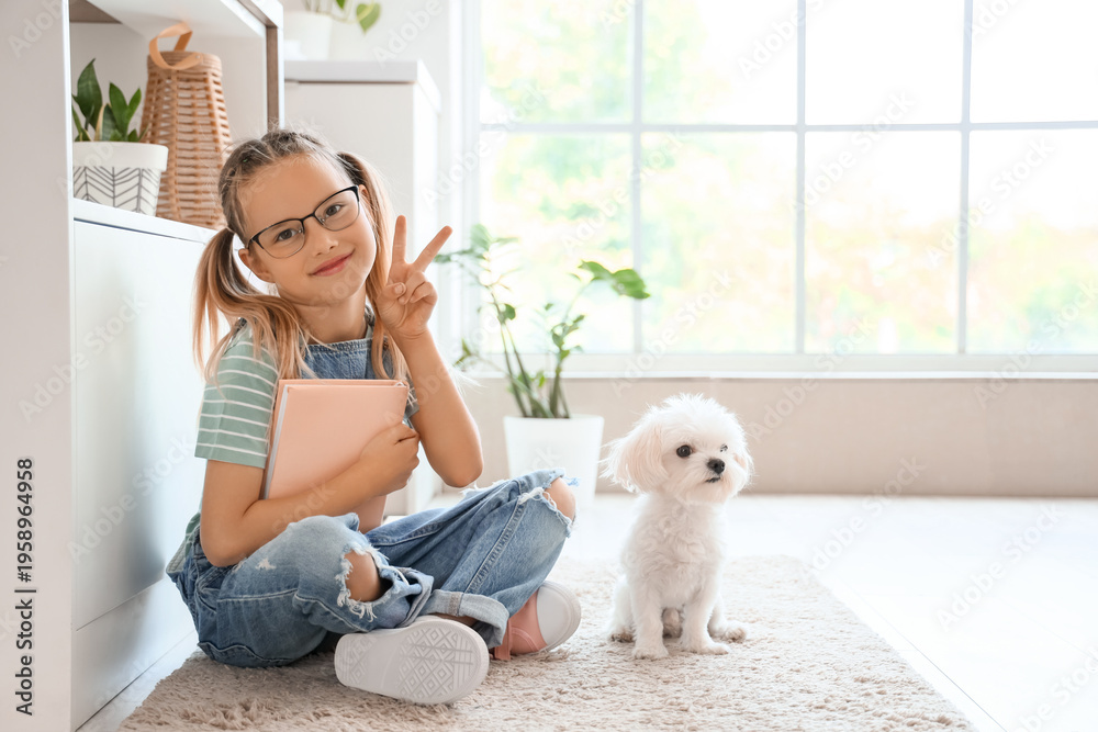 Obraz premium Cute little happy girl with Maltese dog and book sitting on floor in kitchen