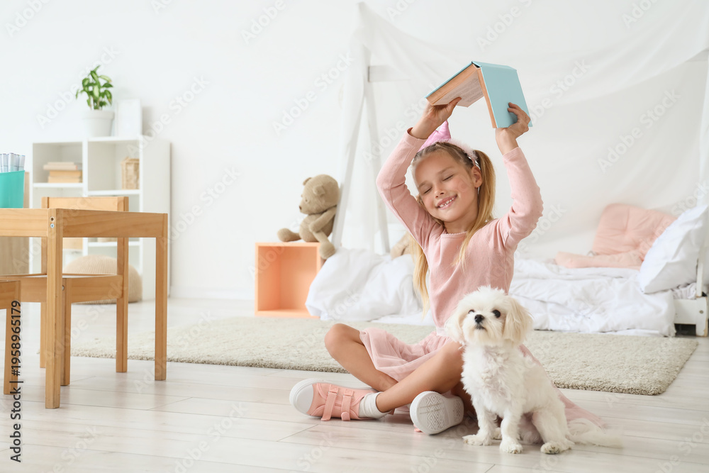Fototapeta premium Cute little happy girl in princess crown with Maltese dog reading book on floor at home
