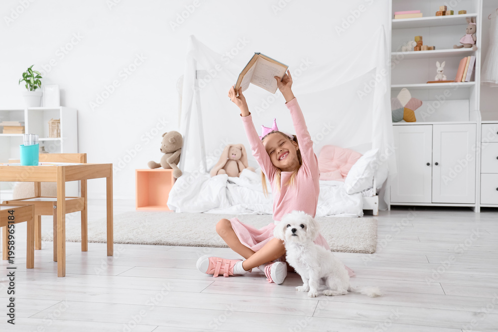 Obraz premium Cute little happy girl in princess crown with Maltese dog reading book on floor at home