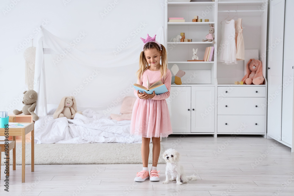 Obraz premium Cute little happy girl in princess crown with Maltese dog reading book at home
