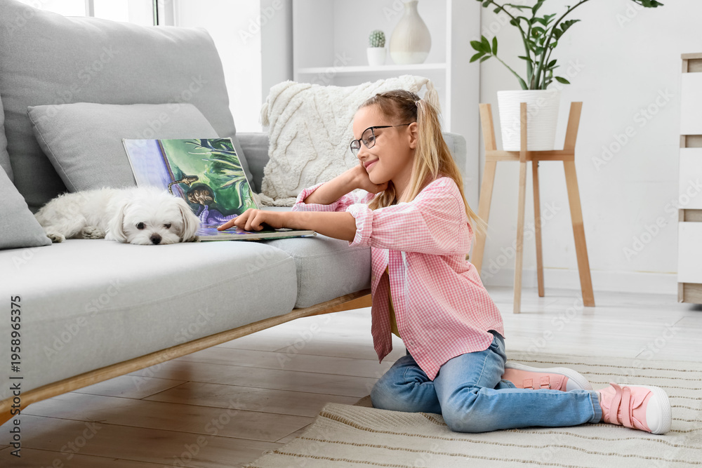 Obraz premium Cute little happy girl with Maltese dog reading book on floor near sofa at home