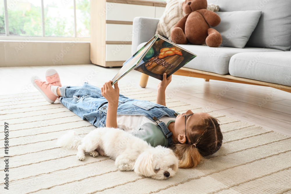 Obraz premium Cute little happy girl with Maltese dog reading book on floor at home