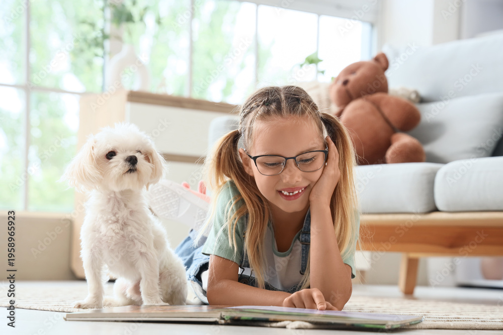 Obraz premium Cute little happy girl with Maltese dog reading book on floor at home