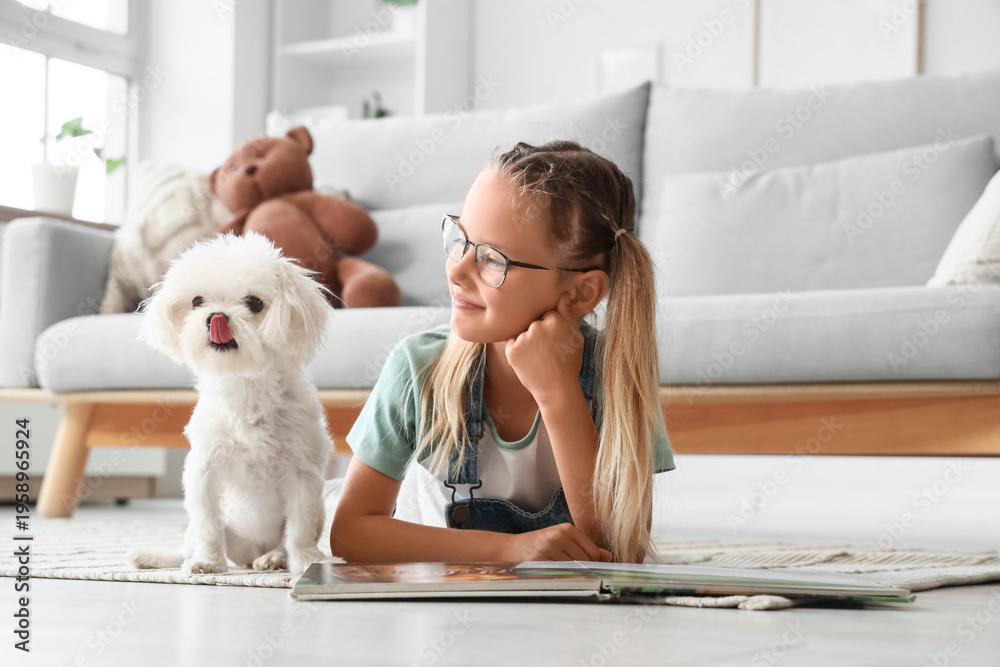 Naklejka premium Cute little happy girl with Maltese dog reading book on floor at home
