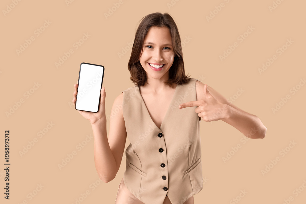 Naklejka premium Beautiful young happy woman in stylish vest pointing at mobile phone on beige background
