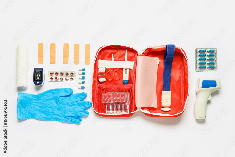Fototapeta premium First aid kit with pills, infrared thermometer and medical patches on white background