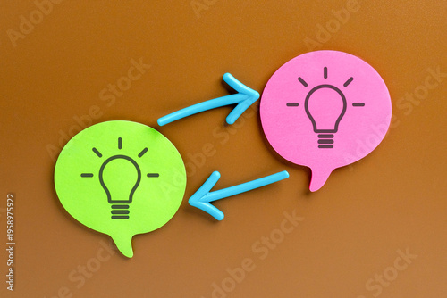 фотографія A flat lay of green and pink speech bubble with lightbulb icons connected by bidirectional arrows