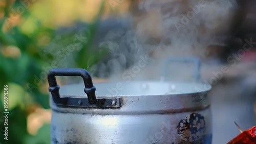 Steam Rising from Metal Pot on Outdoor Table Surrounded by Greenery in a Warm and Inviting Natural Setting