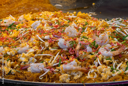 A vibrant close-up of Pad Thai stir-fried in a wok with shrimp, eggs, bean sprouts, and chives, showcasing the rich textures and colors of Thai street food.