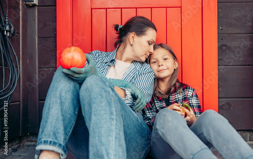 mother and daughter sitting together on porch after gardening holding fresh vegetables smiling and relaxing near red door family bonding countryside lifestyle harvest, homegrown food