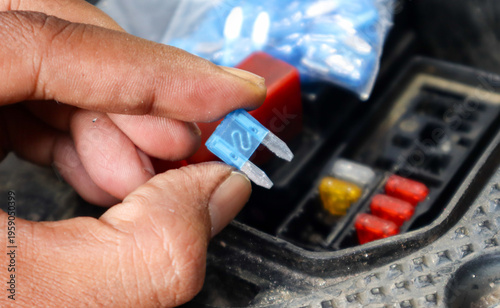 Quadro su tela A close-up of a hand holding a blue automotive fuse, showing its transparent plastic casing and metal connectors, commonly used for circuit protection in vehicles
