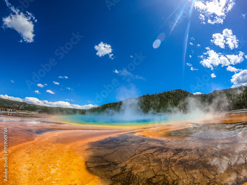 Vibrant hot spring radiates golden hues under bright blue sky