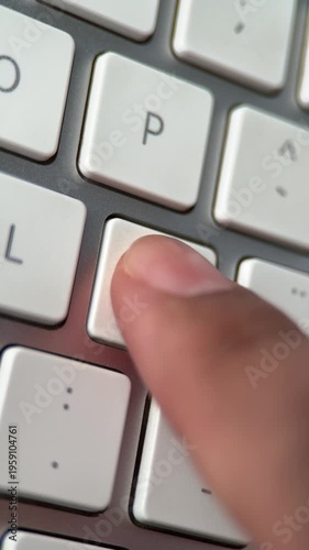 Vertical close up of a Hispanic person's finger repeatedly pressing the Ñ key on a white keyboard, Concept of Spanish language, communication, and digital writing