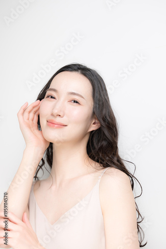 黒髪のパーマのロングヘアで白背景の若い女性のビューティーイメージ　スキンケアなどのツヤ肌、透明感がある保湿や高級感のあるラグジュアリーな美容イメージカメラ目線