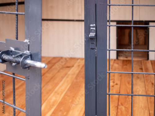 Tableau sur toile Close-up of kennel door latch and metal mesh in dog enclosure, symbolizing security, control and potential escape, with blurred wooden interior and dog house behind
