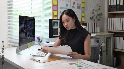 A woman is sitting at a desk with a computer monitor and a keyboard. She is using a stylus to draw on a piece of paper