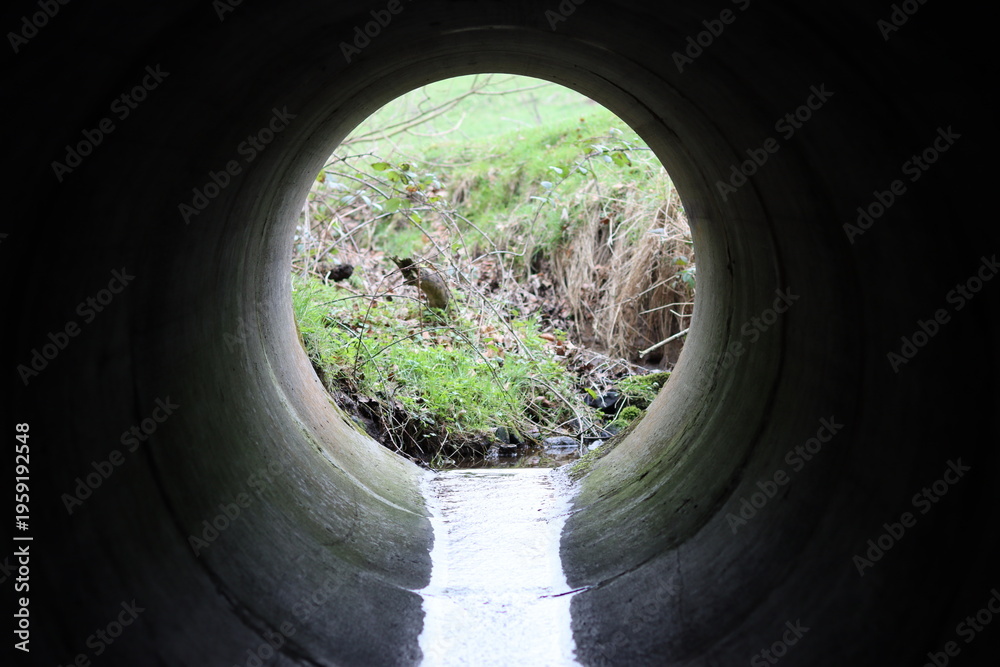 Fototapeta premium View through a round concrete tunnel carrying a stream beneath a road