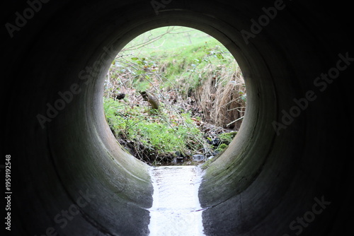 Картината върху платно View through a round concrete tunnel carrying a stream beneath a road