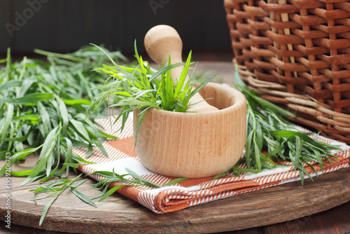 Tarragon spice in a mortarl on wooden rustic background with fresh leaves nearby, copy space, natural medicine,  natural hair and skin treatment, aromatherapy concept