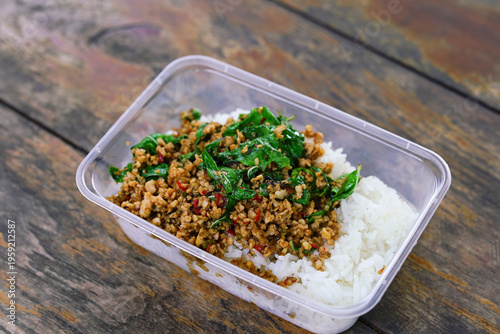 Stir-fried minced pork with basil leaves, served with rice in a plastic container.