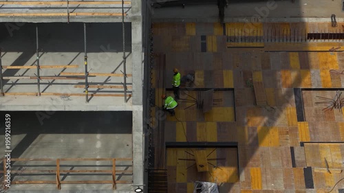 Aerial drone shot looking straight down at two construction workers installing steel reinforcement on formwork deck, showcasing structural preparation and active building process.