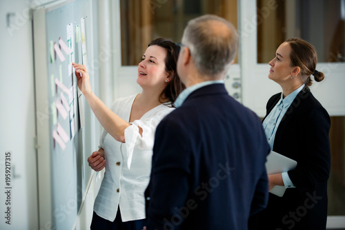 Smiling female mentor presenting project results on a whiteboard to her professional team. Positive corporate culture, successful leadership concept.