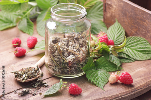 Dry raspberry leaf tea in glass jar with leaves and berry on rustic background, natural green medicine for menopause, pms, pregnancy, woman drink concept