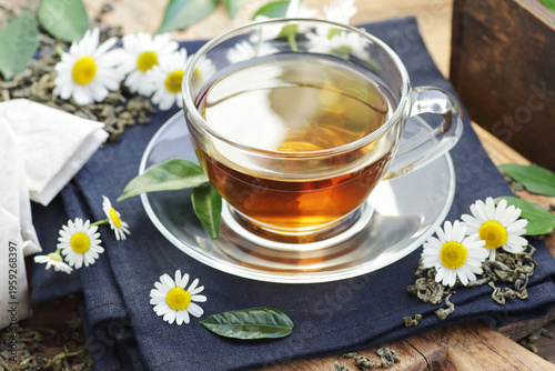 Green chinese tea with camomile flowers and fresh leaves, hot drink on black background, closeup, natural medicine and naturopathy concept